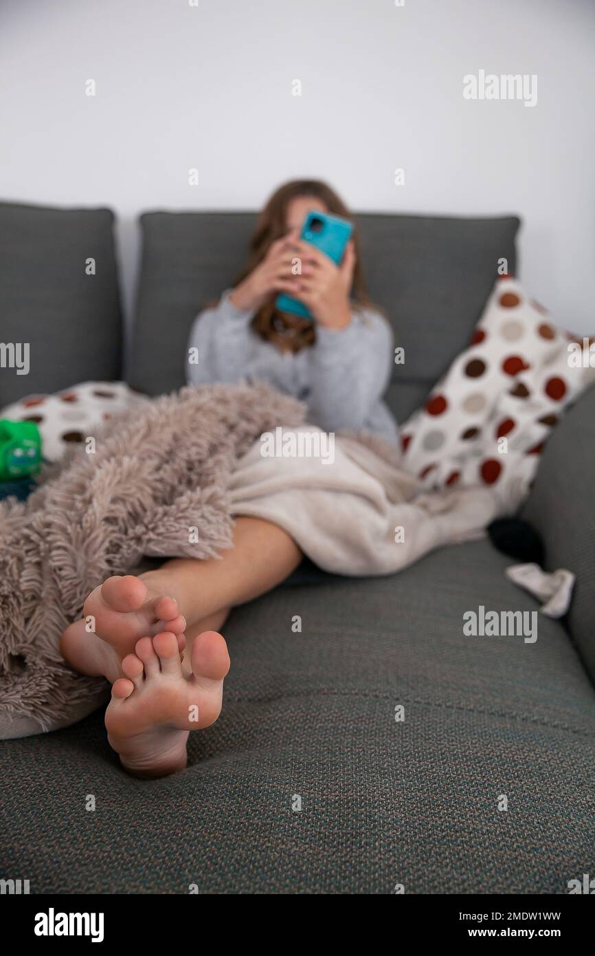 Young girl, teen, preteen, sitting on a large long canape sofa. Visibly bored, center of focus is on her feet that are in front of the camera. Spendin Stock Photo