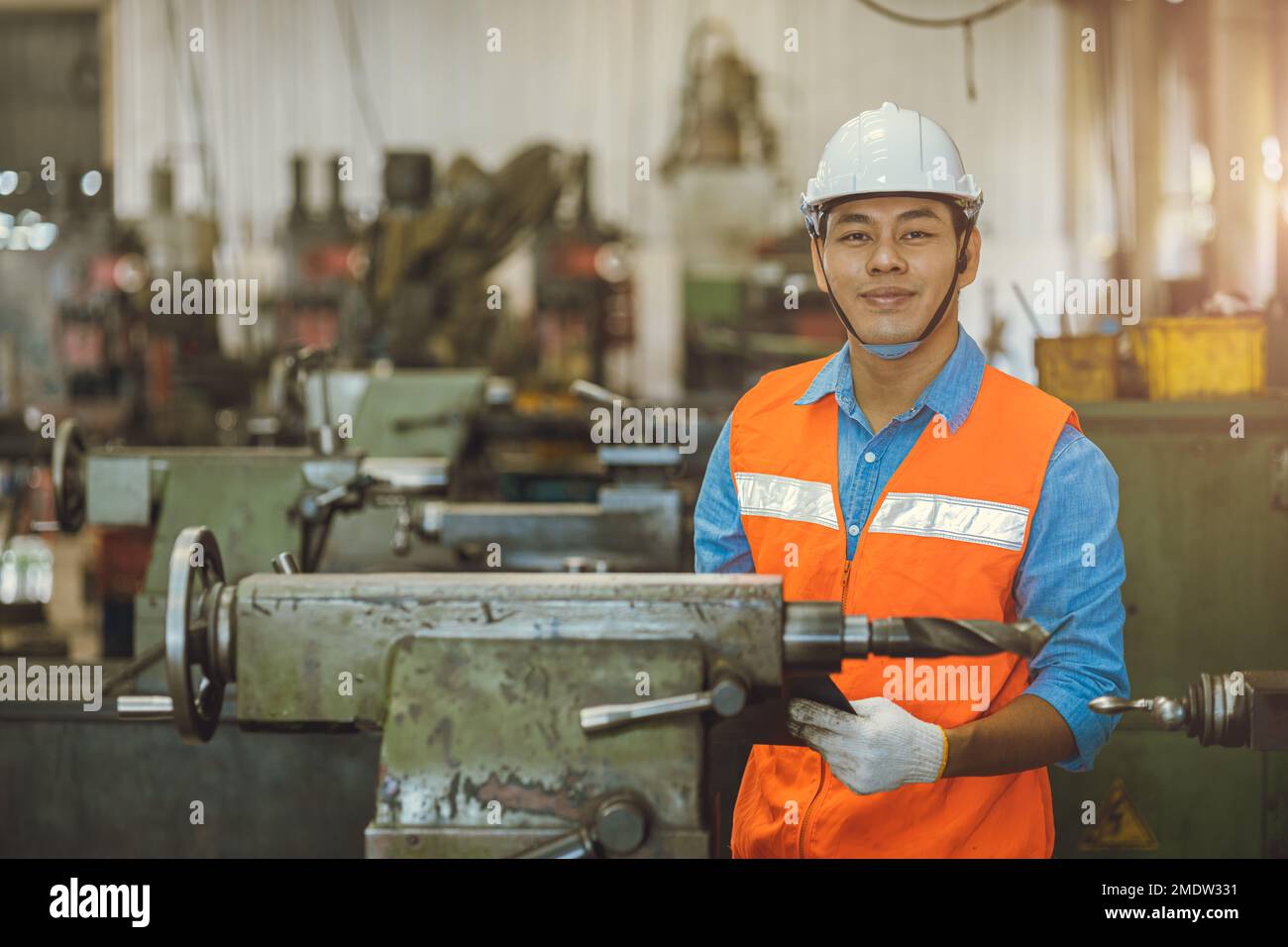 portrait Asian engineer adult male worker in machine shop with check list happy smile in safety hardhat Stock Photo