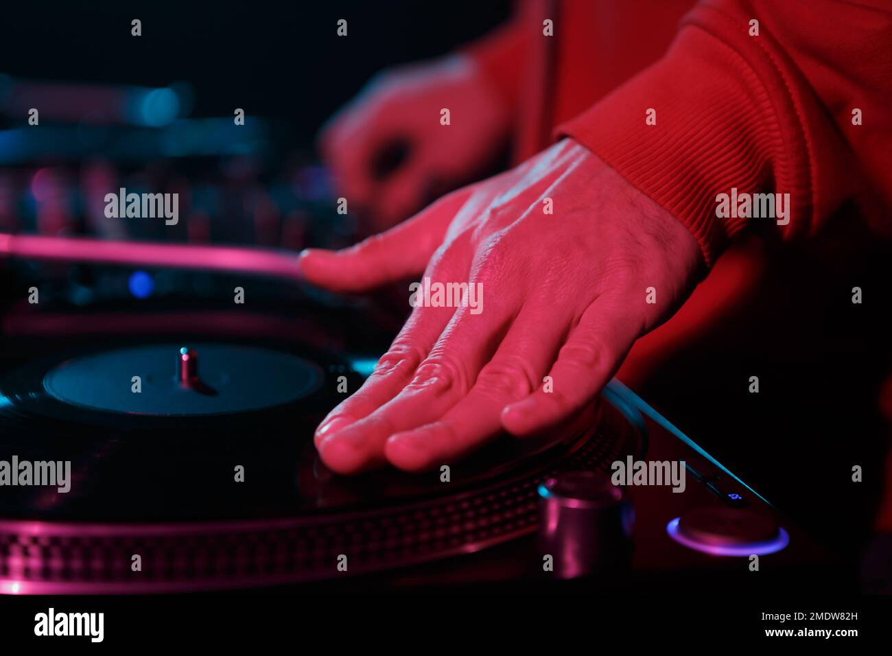 Hip hop DJ scratches vinyl disc on turntable in red stage lights. Hand