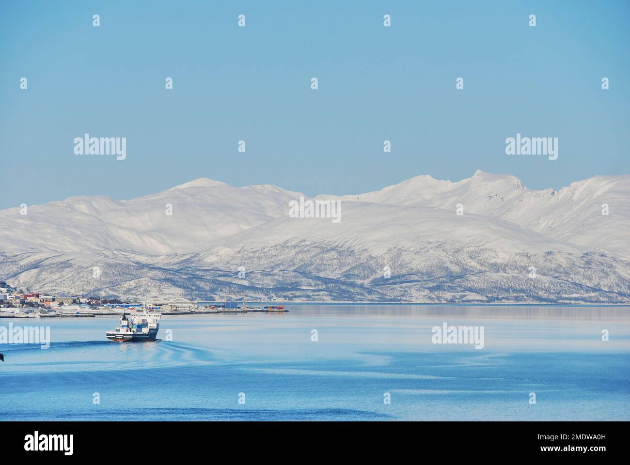 fishing boat in the winter landscape of the port of Tromso in a fjord at the coastline of northern Norway with snow covered mountains in the backgroun Stock Photo
