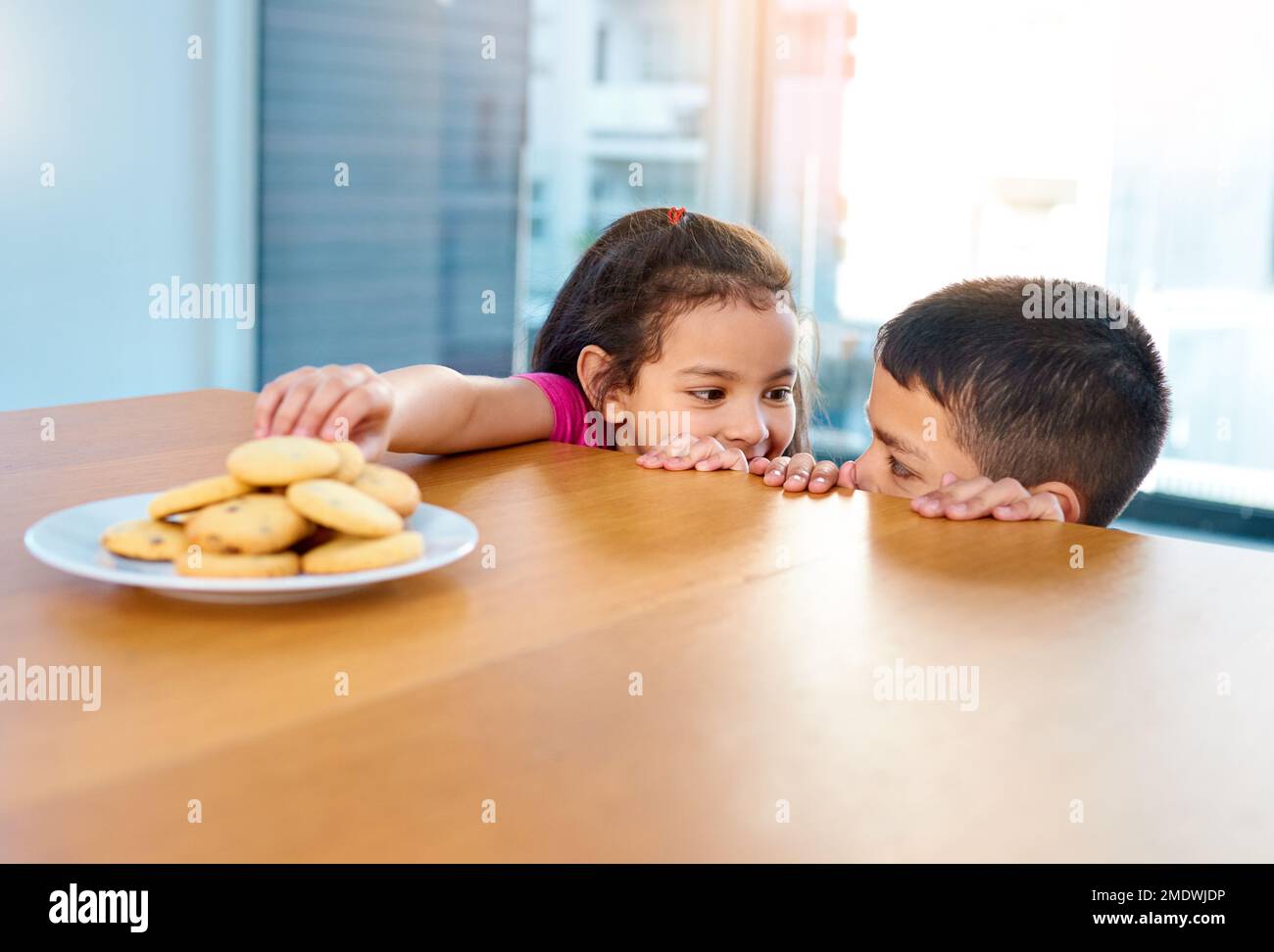 Dont tell anyone about this okay. two mischievous young children stealing cookies on the kitchen table at home. Stock Photo