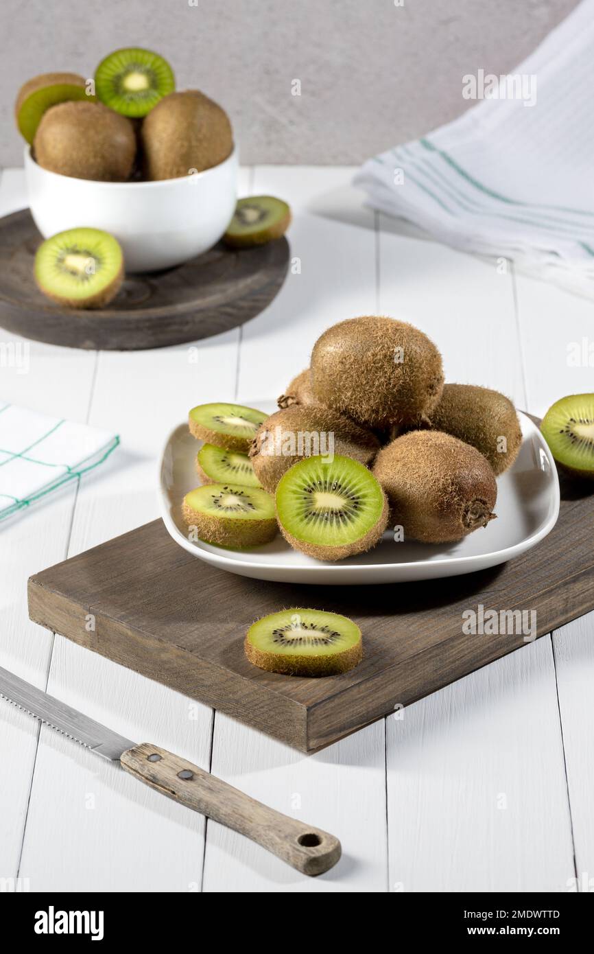 Fresh kiwi and slices on white plate on white wood base. Vertical format. Stock Photo