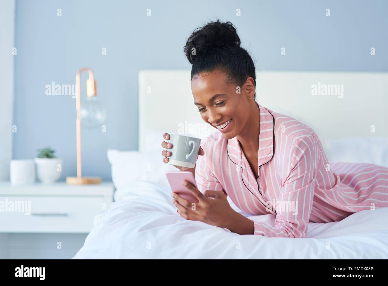 Time to catch up on some hot gossip. an attractive young woman drinking coffee while using her cellphone in bed at home. Stock Photo