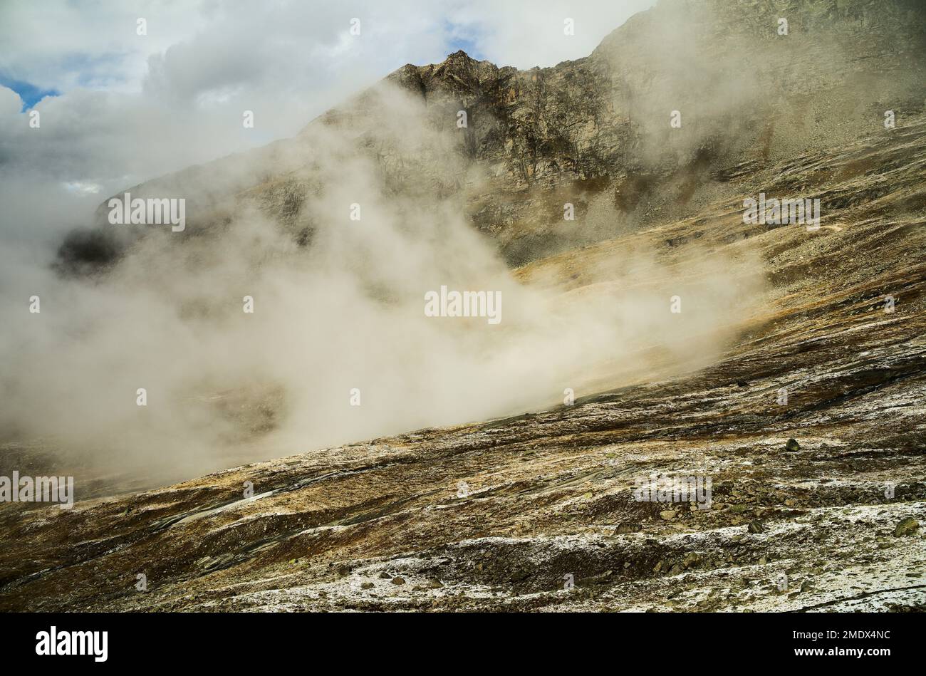The hot steam and geysers coming out of a mountain with the cloudy sky in the background Stock Photo