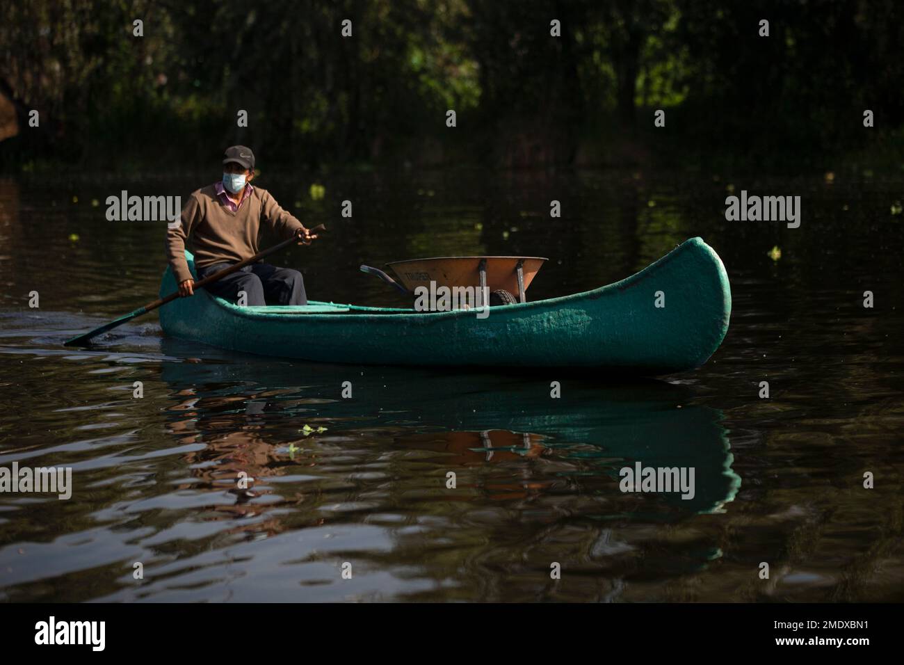 A farmer carries a wheelbarrow in his canoe as e paddles to his farm