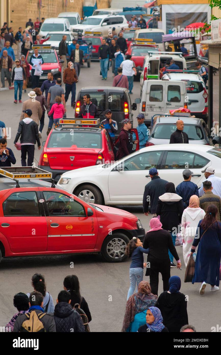 Fez, Morocco - traffic of pedestrians, cars, red petit taxis on the street outside car-free Fes el Bali medina. Busy drop-off point. Vibrant cityscape. Stock Photo