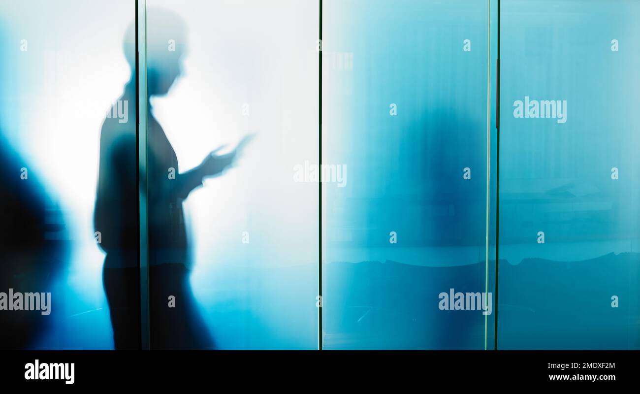 Glass wall, email and businessman reading on a phone for contact, communication and work. Silhouette, social media and employee typing on a mobile Stock Photo