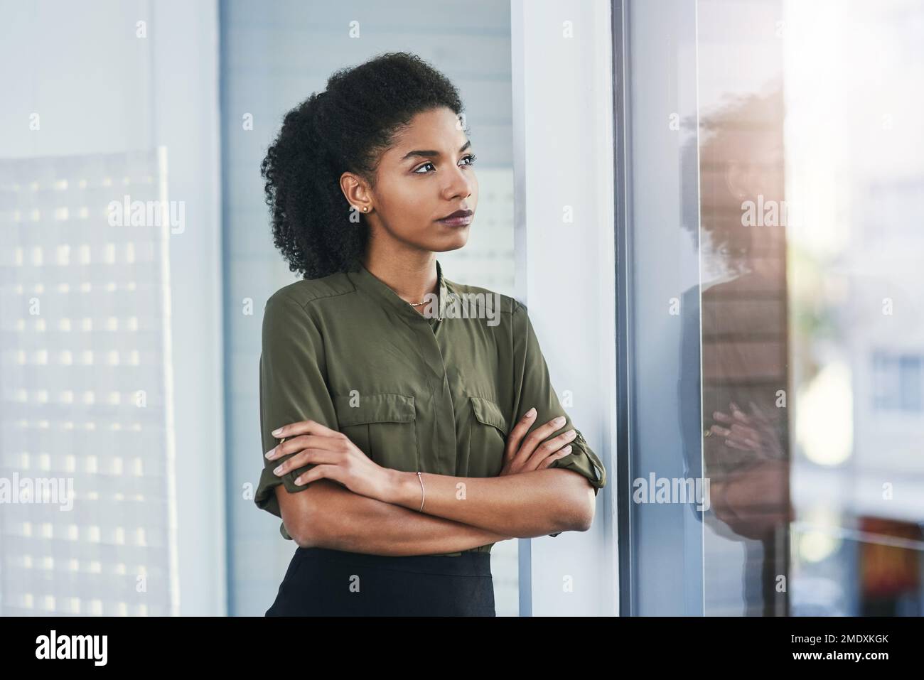 Nothing is impossible when you put your mind into it. a young businesswoman looking out of a window in her office. Stock Photo