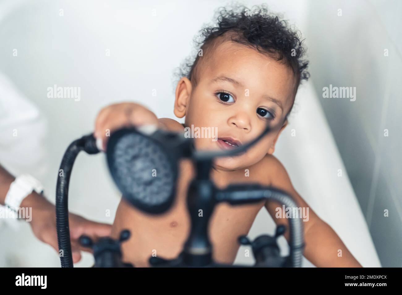 Toddler boy inside a bath tube with a shower head. High quality photo