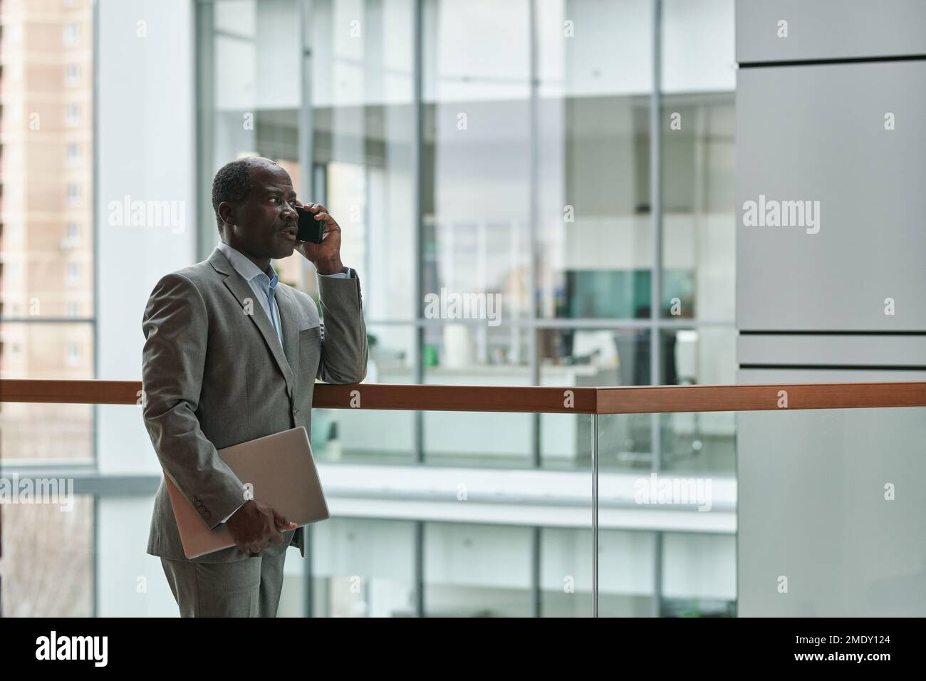 Mature confident African American male entrepreneur in elegant grey suit talking on smartphone to one of subordinates in office center Stock Photo