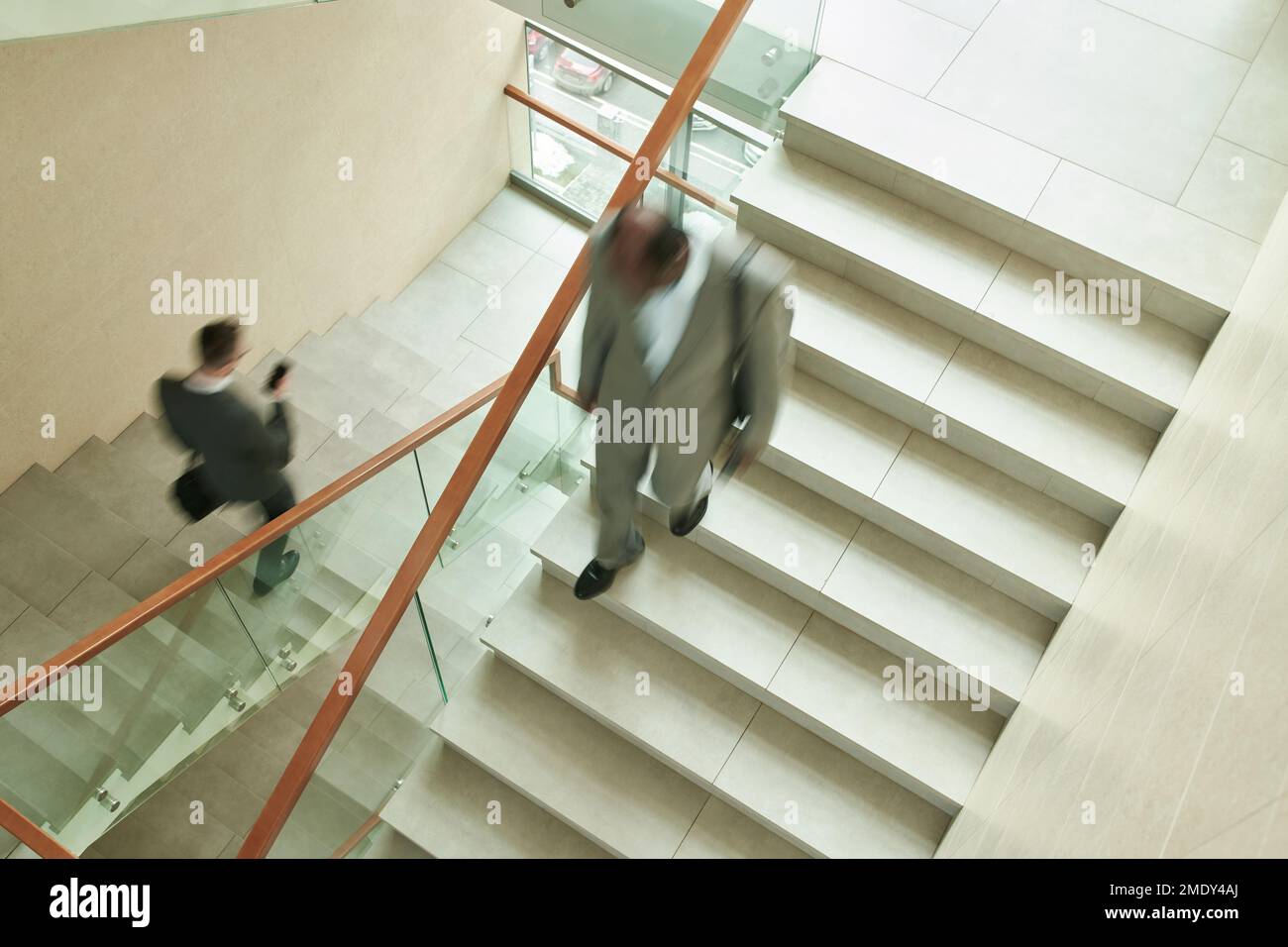 Blurred motion of two multicultural male employees in formalwear walking downstairs along staircase while leaving office center after work Stock Photo