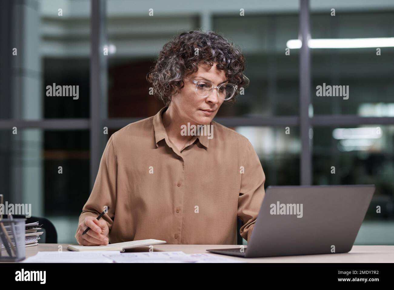 Serious mature financial director of modern business company sitting by workplace and looking through online data on laptop screen Stock Photo