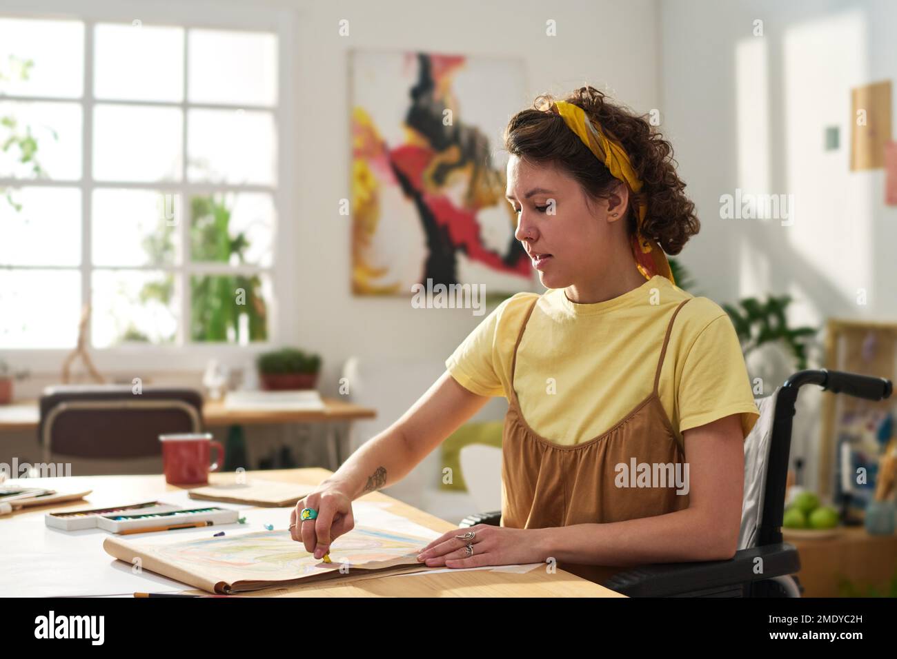 Young craftswoman with disability sitting in wheelchair by table and