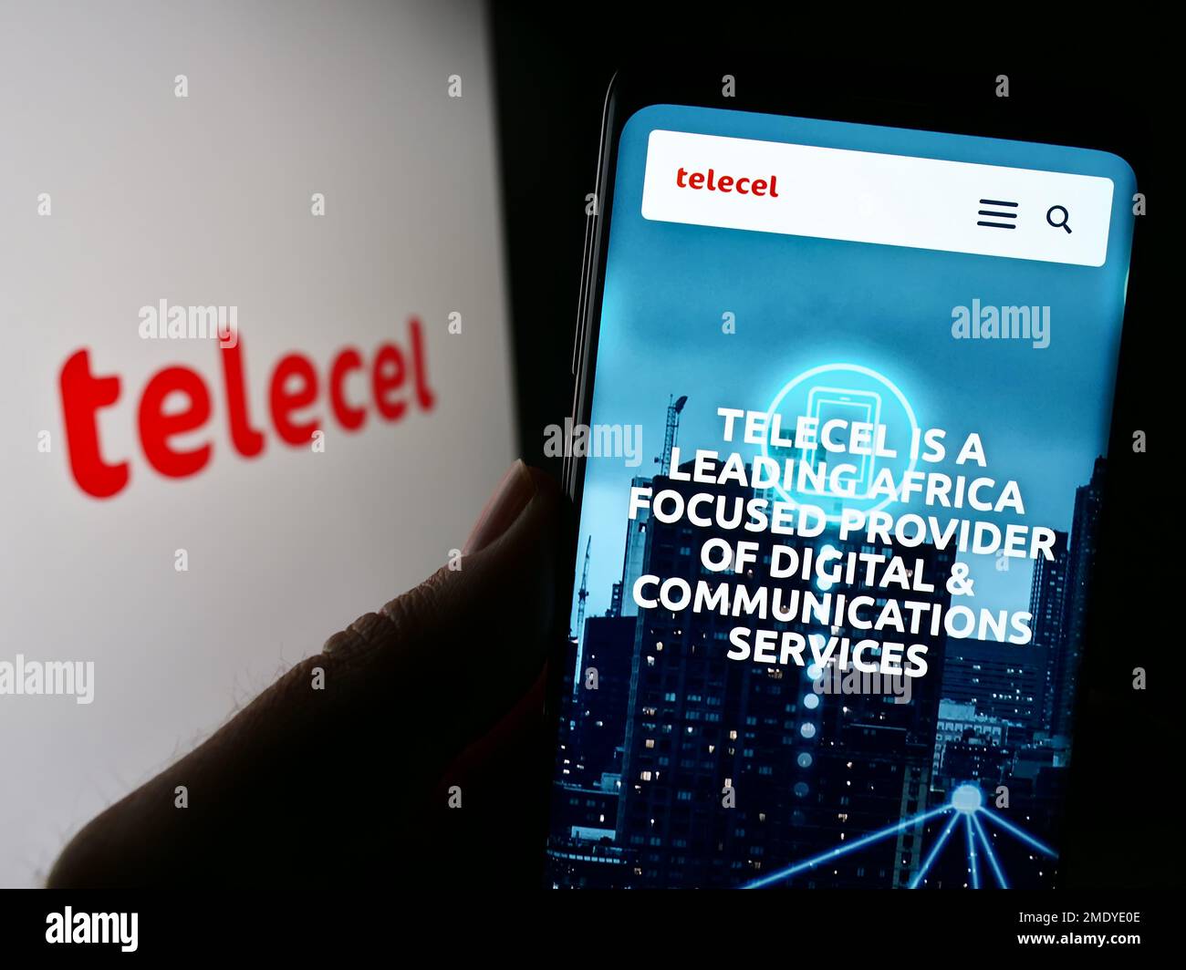 Person holding cellphone with website of telecommunications company Telecel Group on screen in front of logo. Focus on center of phone display. Stock Photo
