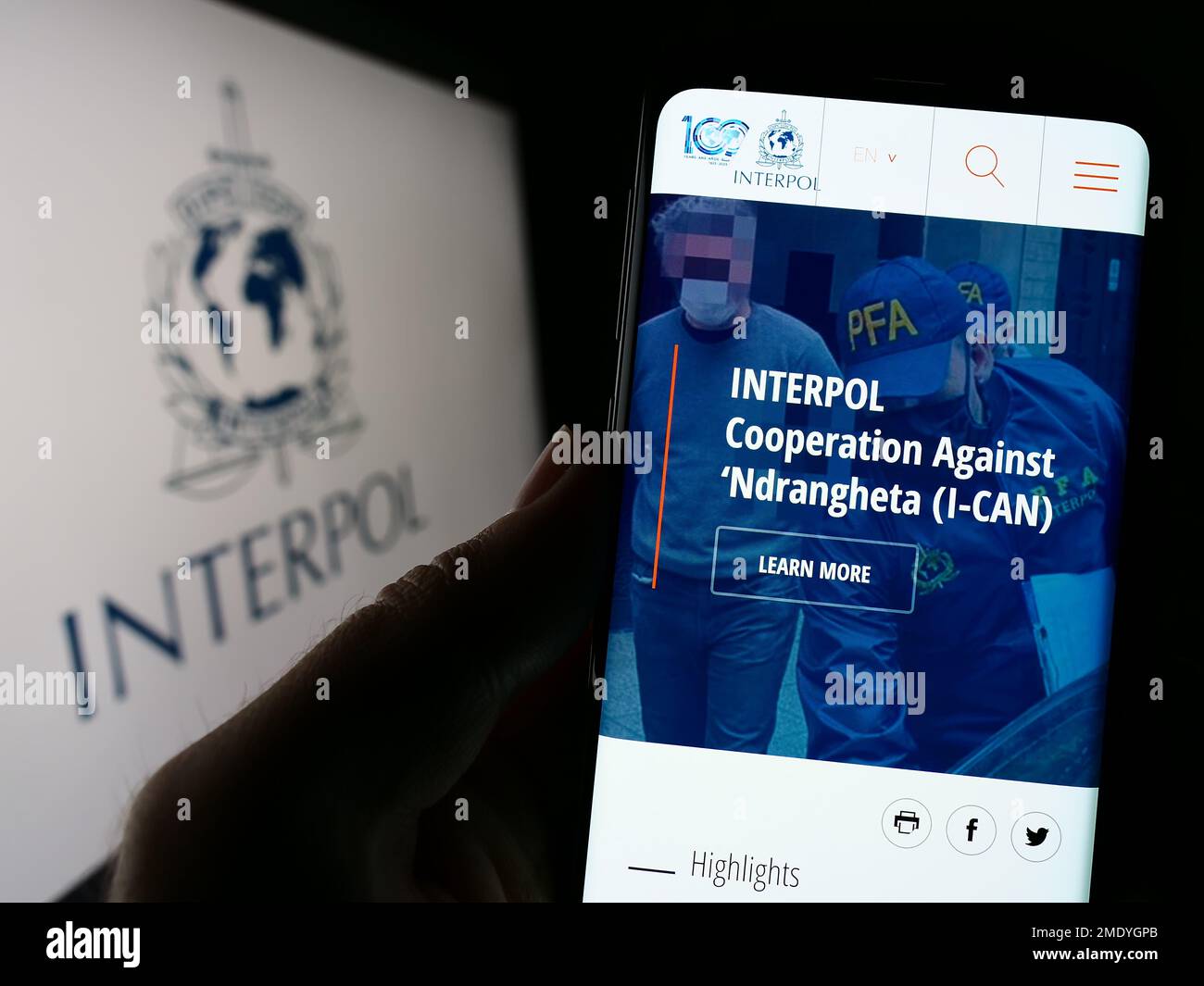 Person holding cellphone with webpage of International Criminal Police Organization (ICPO) on screen with logo. Focus on center of phone display. Stock Photo