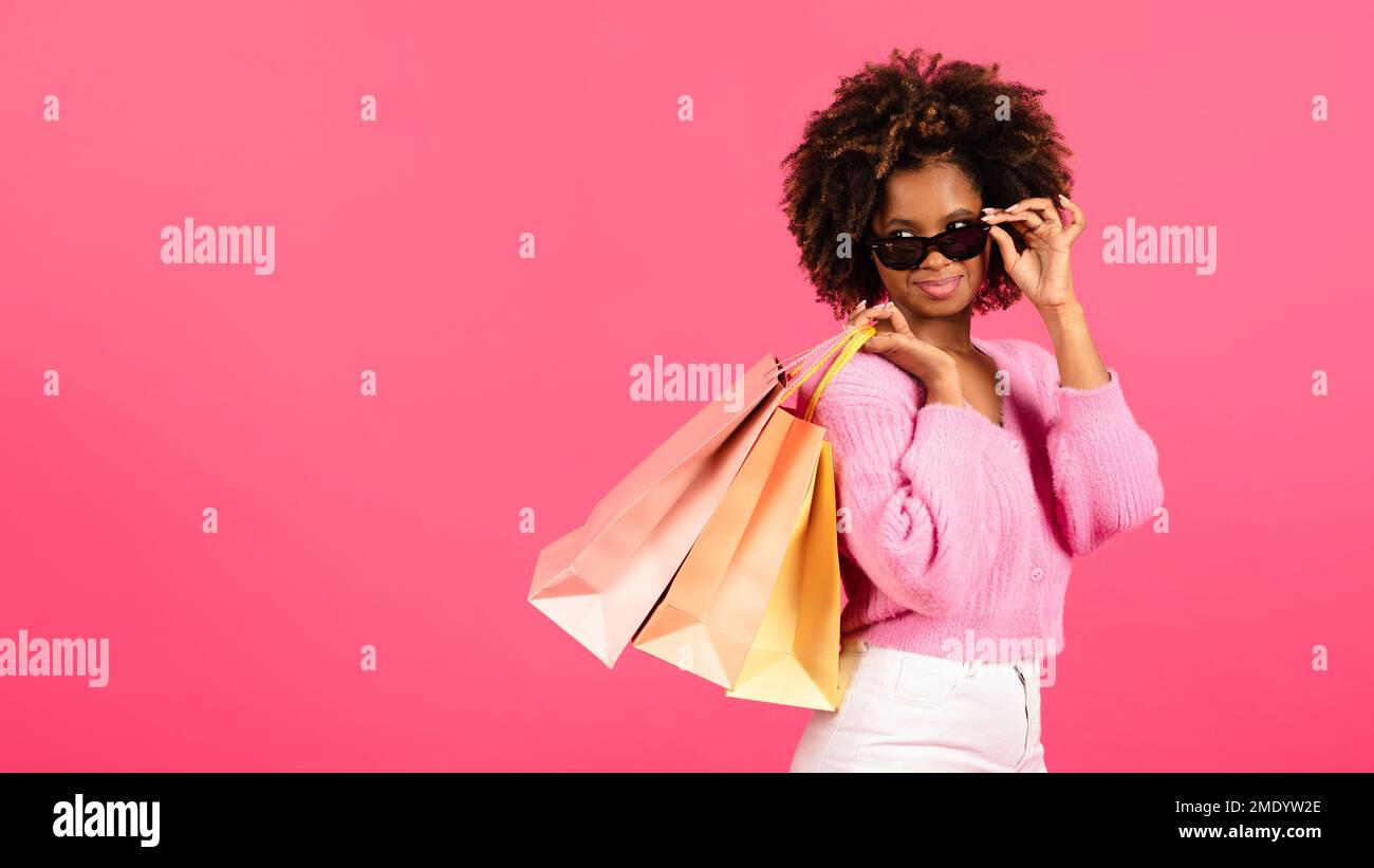 Cheerful millennial african american curly female shopaholic takes off glasses hold many packages Stock Photo