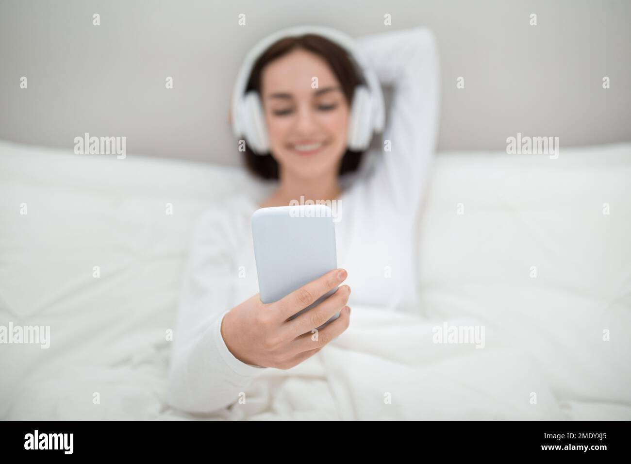 Mobile phone in young woman hand, bedroom interior Stock Photo