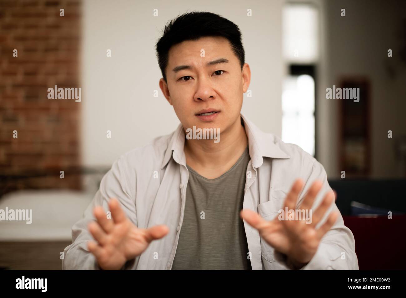 Portrait of asian middle aged man looking at camera and gesturing, communicating via video call, webcam view Stock Photo