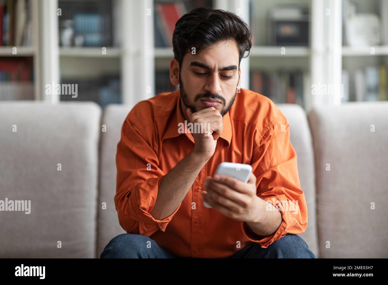 Thoughtful handsome middle eastern man using phone at home Stock Photo
