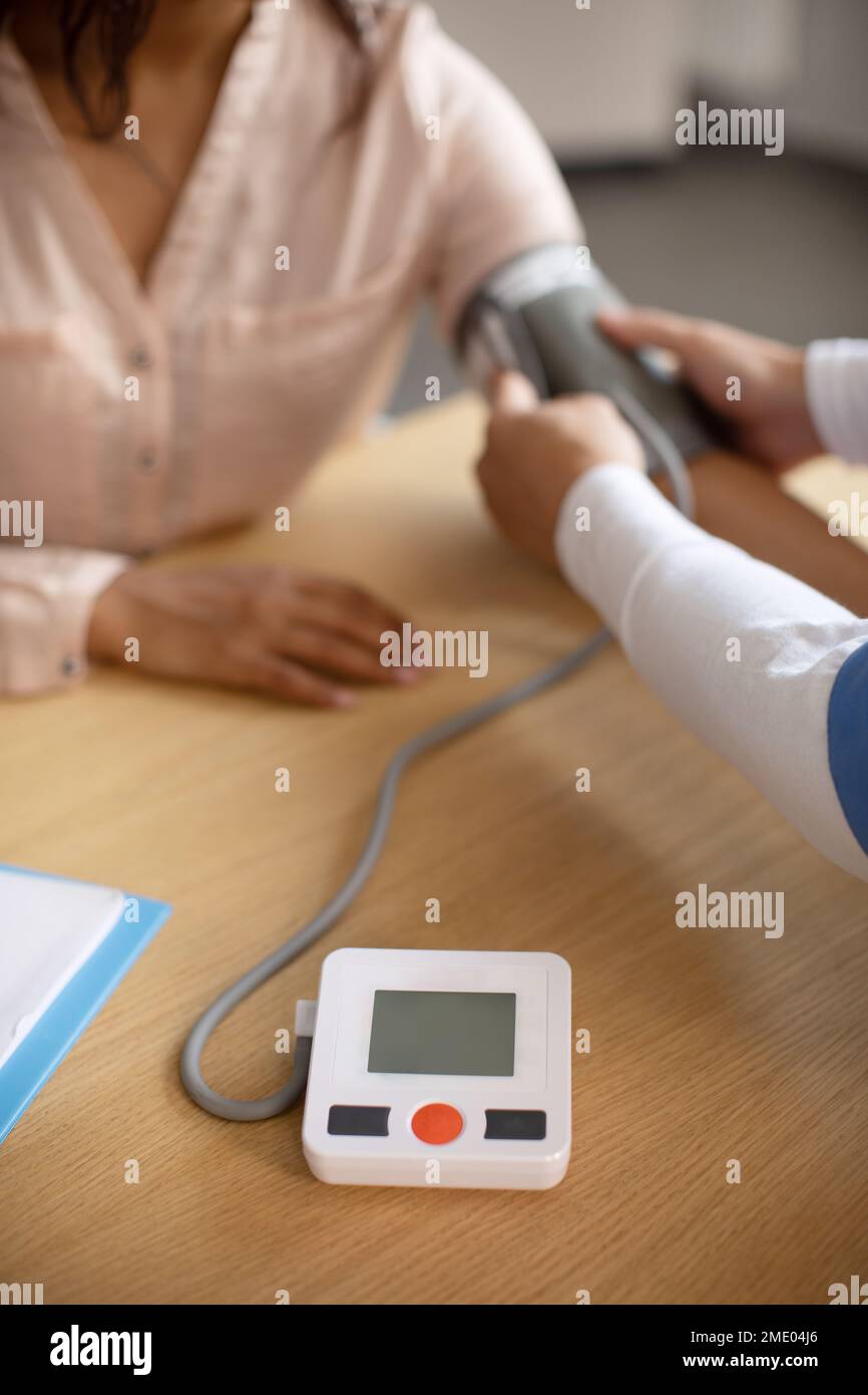 Middle aged korean doctor measures blood pressure with tonometer of young black female patient Stock Photo