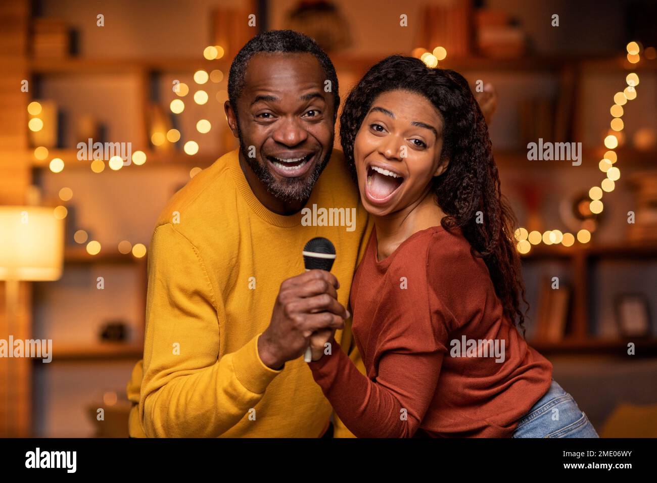 Funny black couple enjoying singing karaoke at home Stock Photo