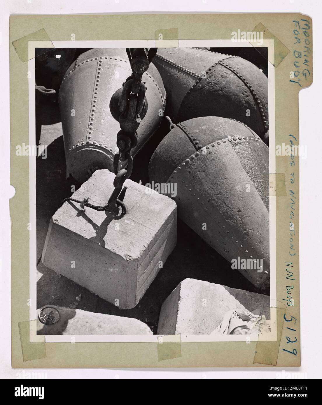 Preparing A Mooring For A Buoy. Buoys which mark the channels are held on their stations by long lengths of chain and concrete sinkers. Here one of the sinkers is about to be lifted from the deck of a Coast Guard cutter. One of the buoys in the background will soon be floating above it. Stock Photo