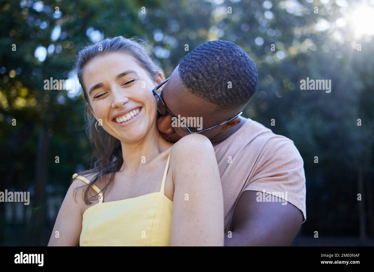 Love, park and kissing with an interracial couple bonding outdoor together on a romantic date in nature. Summer, romance and diversity with a man and Stock Photo