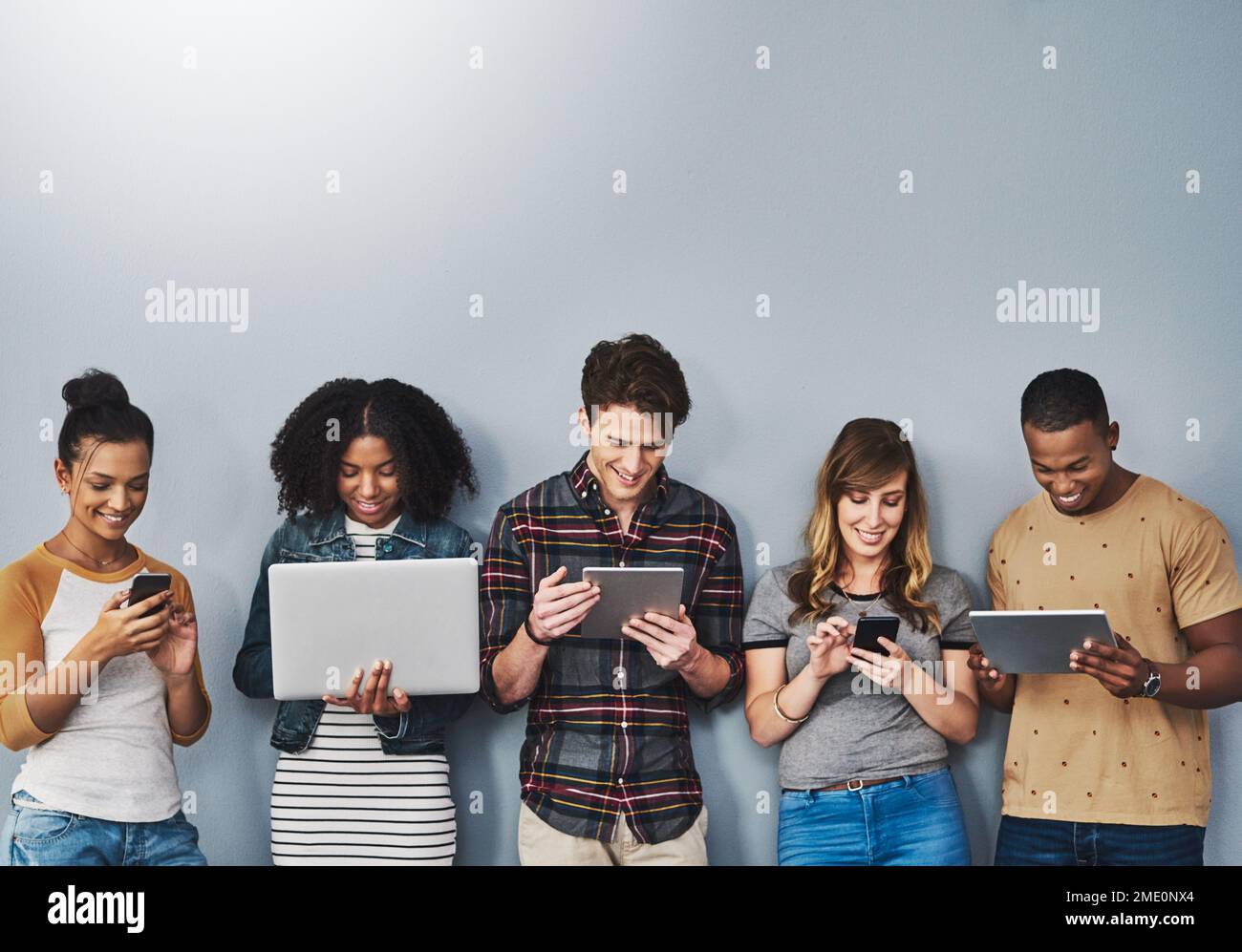 Teched out youth of today. Studio shot of a group of young people using wireless technology against a gray background. Stock Photo