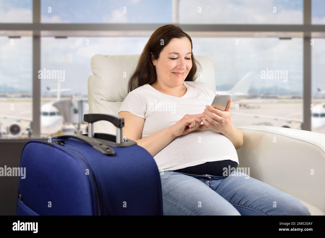 Pregnant woman texting with a smart phone and waiting for her flight in a VIP area and VIP zone aiport Stock Photo