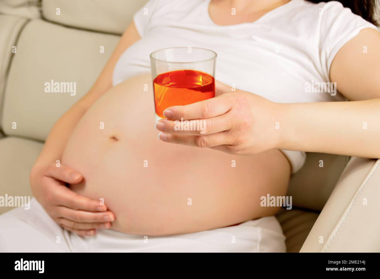 Shot of a woman drinking whiskey while preganant at home Stock Photo