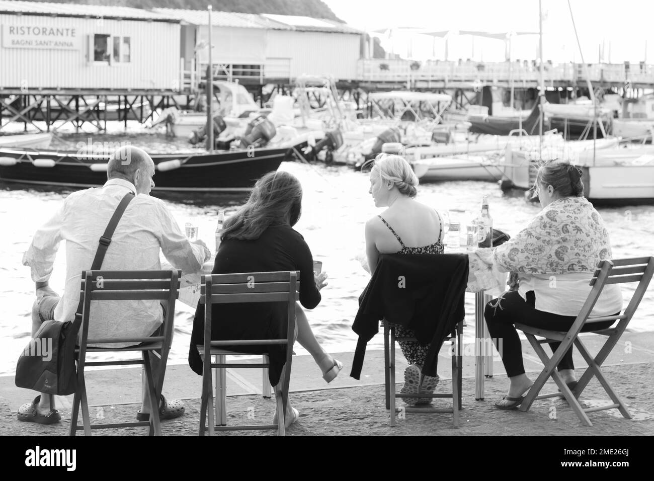 Four people sitting on chairs enjoying a drink at Marina Grande in Sorrento, Campania, Italy. Stock Photo