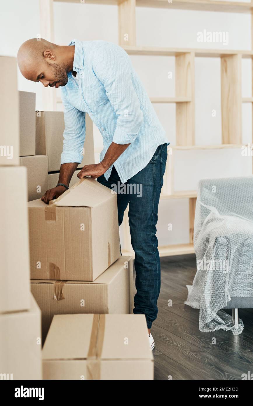 Time to get through some unpacking. a young man unpacking boxes while moving house Stock Photo