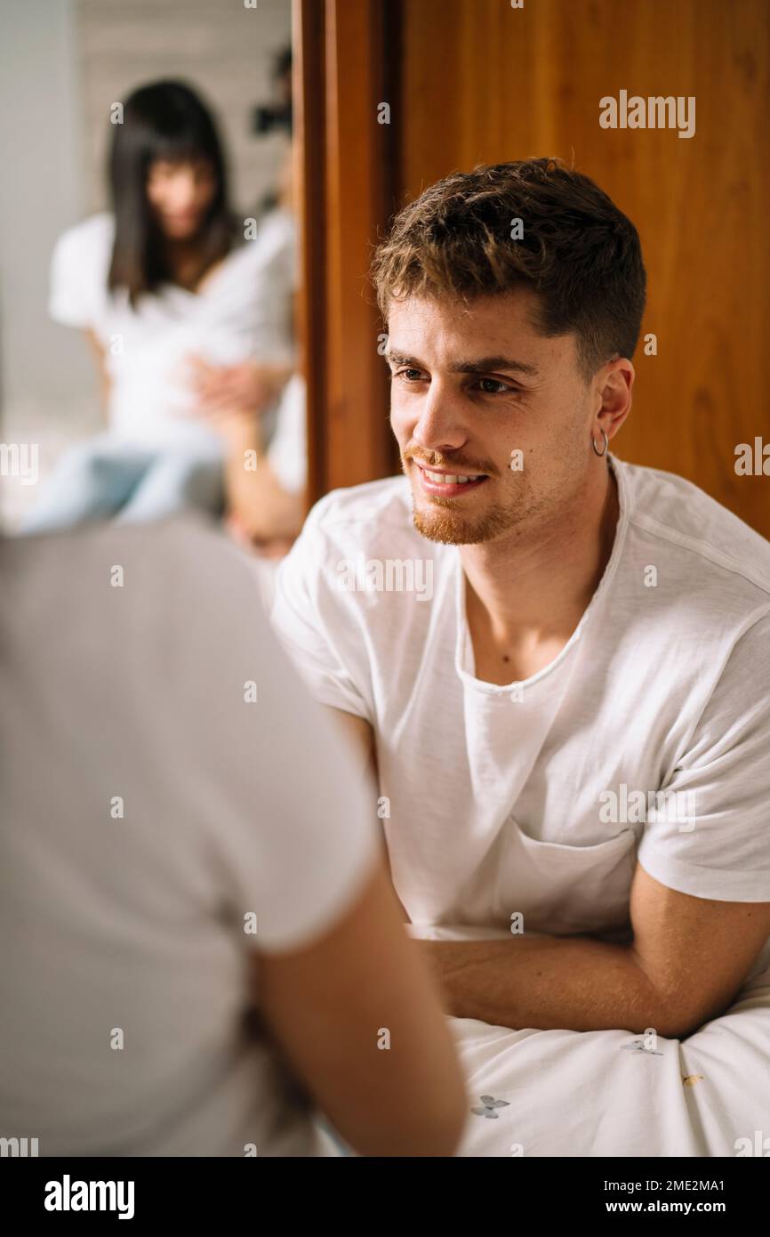 Reflection in mirror of happy young man giving hand to pregnant