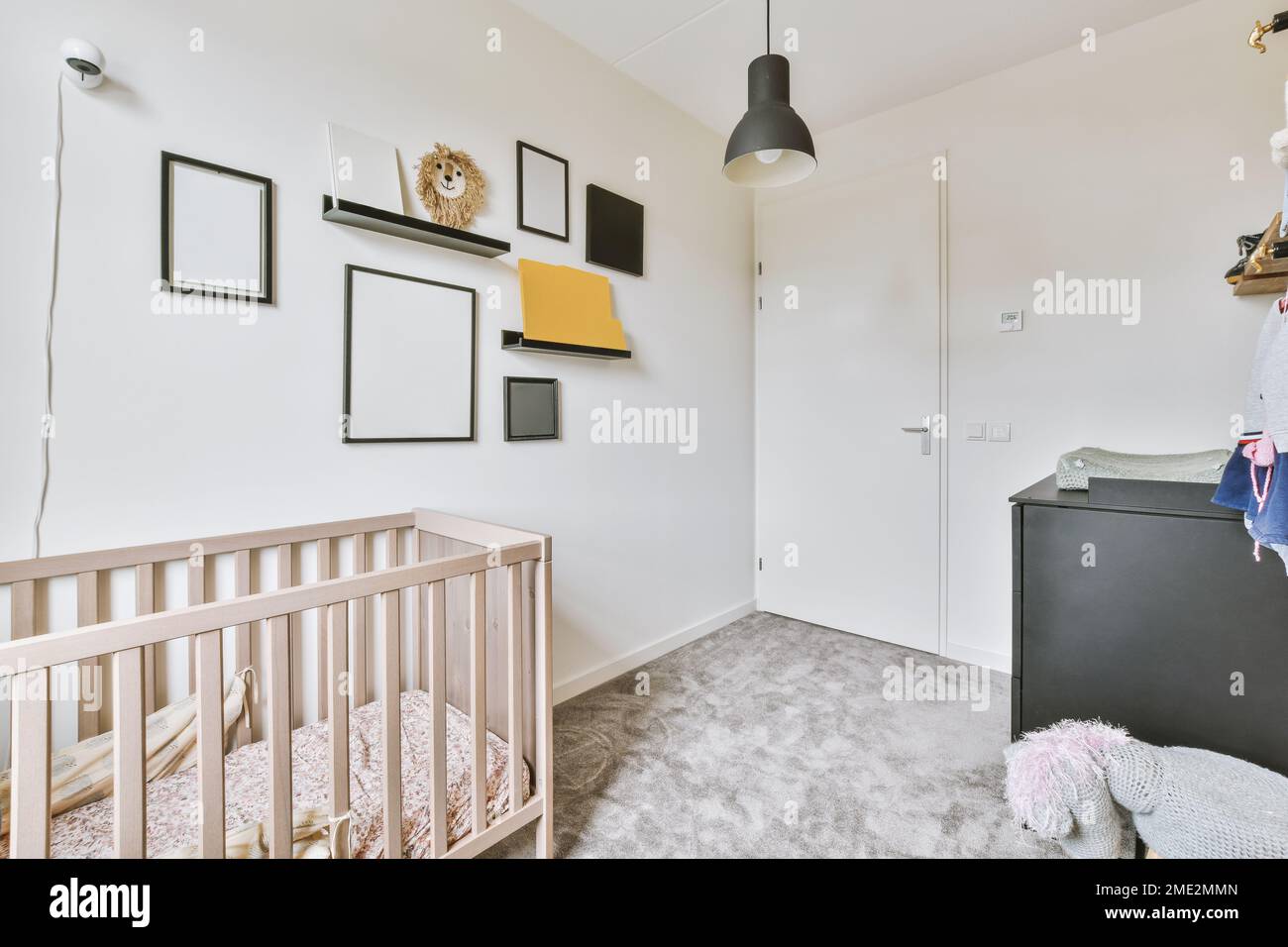 Empty frames and shelf with handicraft hanging on wall over crib in light nursery Stock Photo