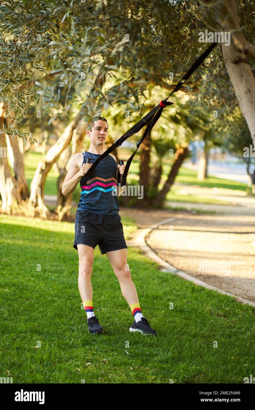 Full body male athlete exercising with TRX straps attached to tree