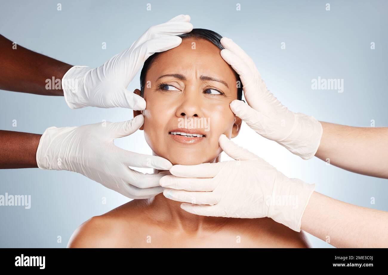 Plastic surgery, confused and face of woman with hands from doctors isolated on blue background. Skincare, check and senior person worried about botox Stock Photo