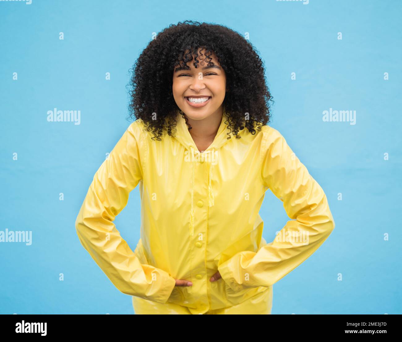 Black woman, smile and happiness in portrait with rain coat,.fashion for winter and beauty isolated on blue background. Happy in studio, style and Stock Photo