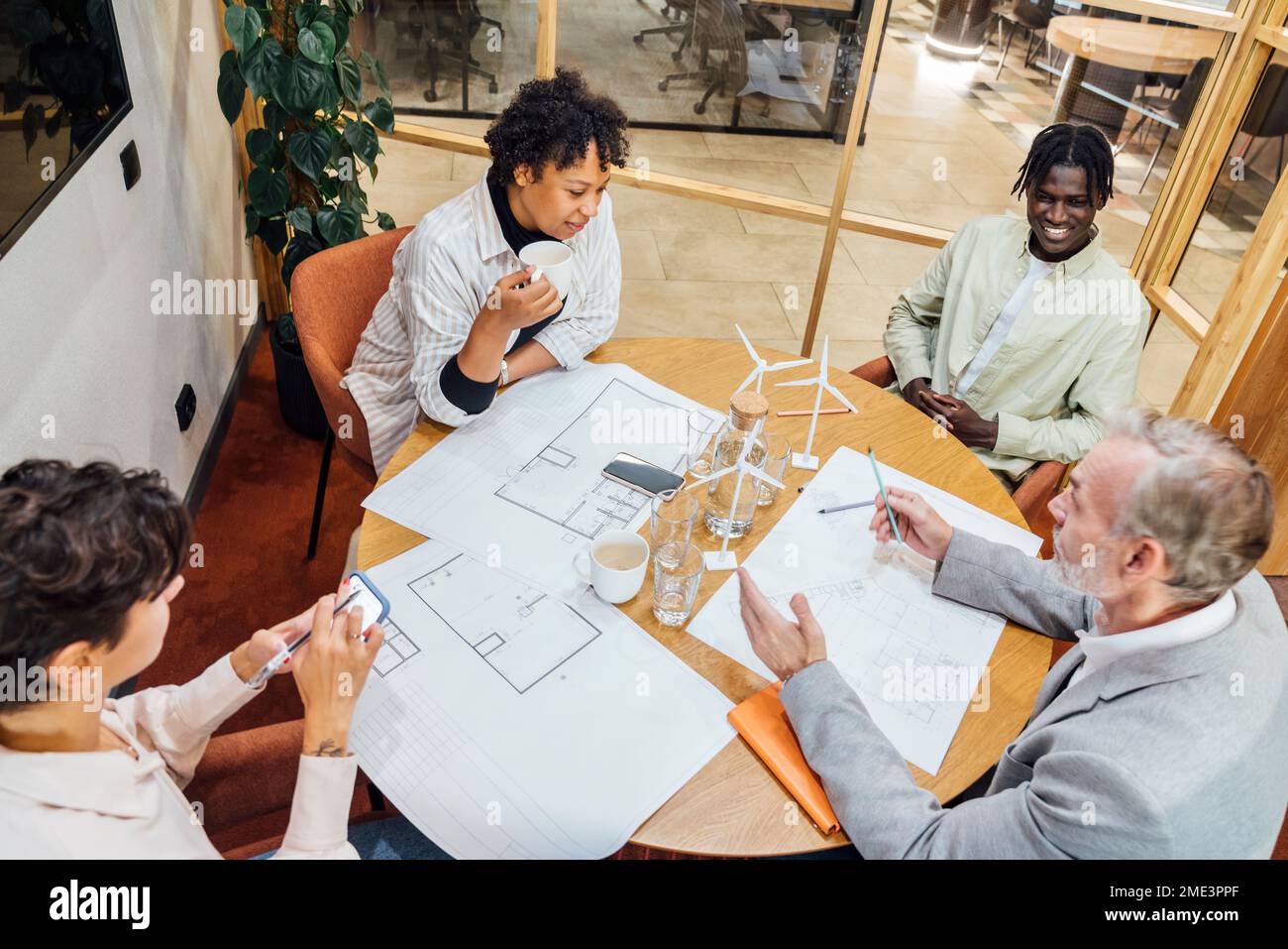 Mature businessman discussing over blueprints and wind turbine models with colleagues in office Stock Photo