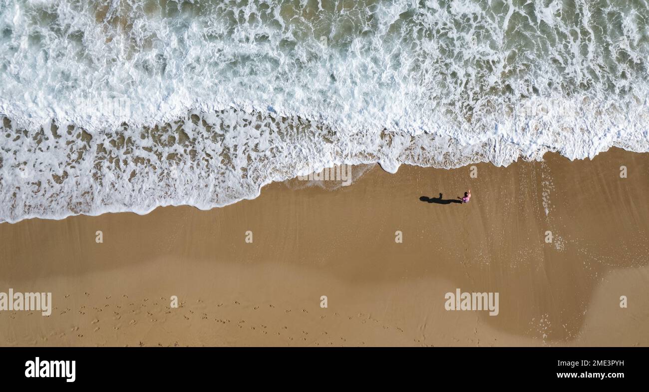 Aerial drone point of view unrecognised child play on sand in a beach. Stormy waves idyllic beach in winter. Protaras, Cyprus Stock Photo