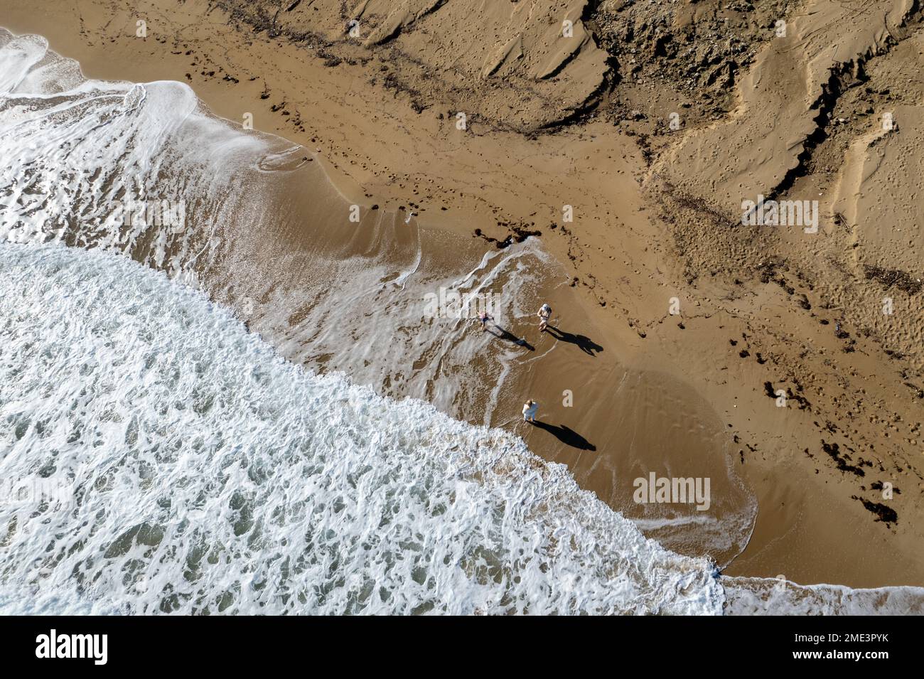 Aerial drone point of view of people walking on sand in a beach. Stormy waves idyllic beach in winter. Stock Photo
