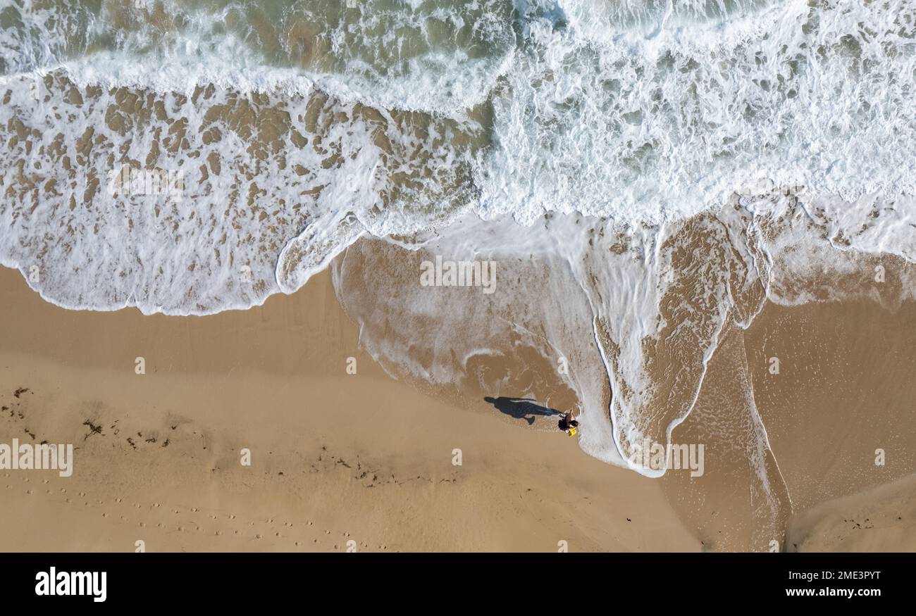 Aerial drone point of view of person walking on sand in a beach. Stormy waves idyllic beach in winter. Stock Photo