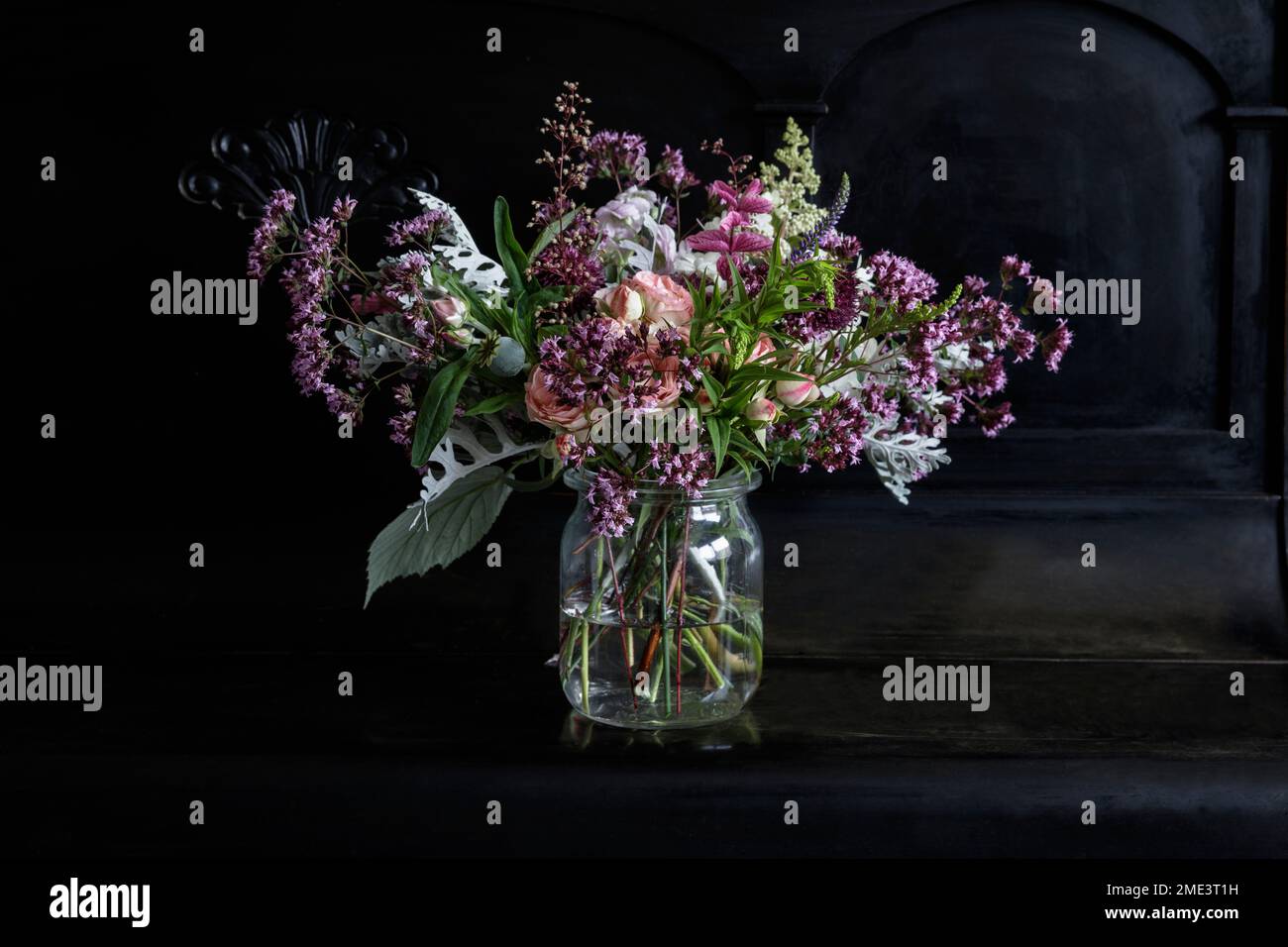 Bunch of flowers in glass jar on black piano Stock Photo