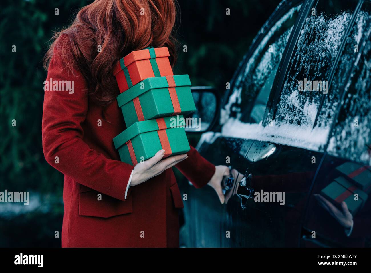 Redhead woman with Christmas gifts standing by car Stock Photo