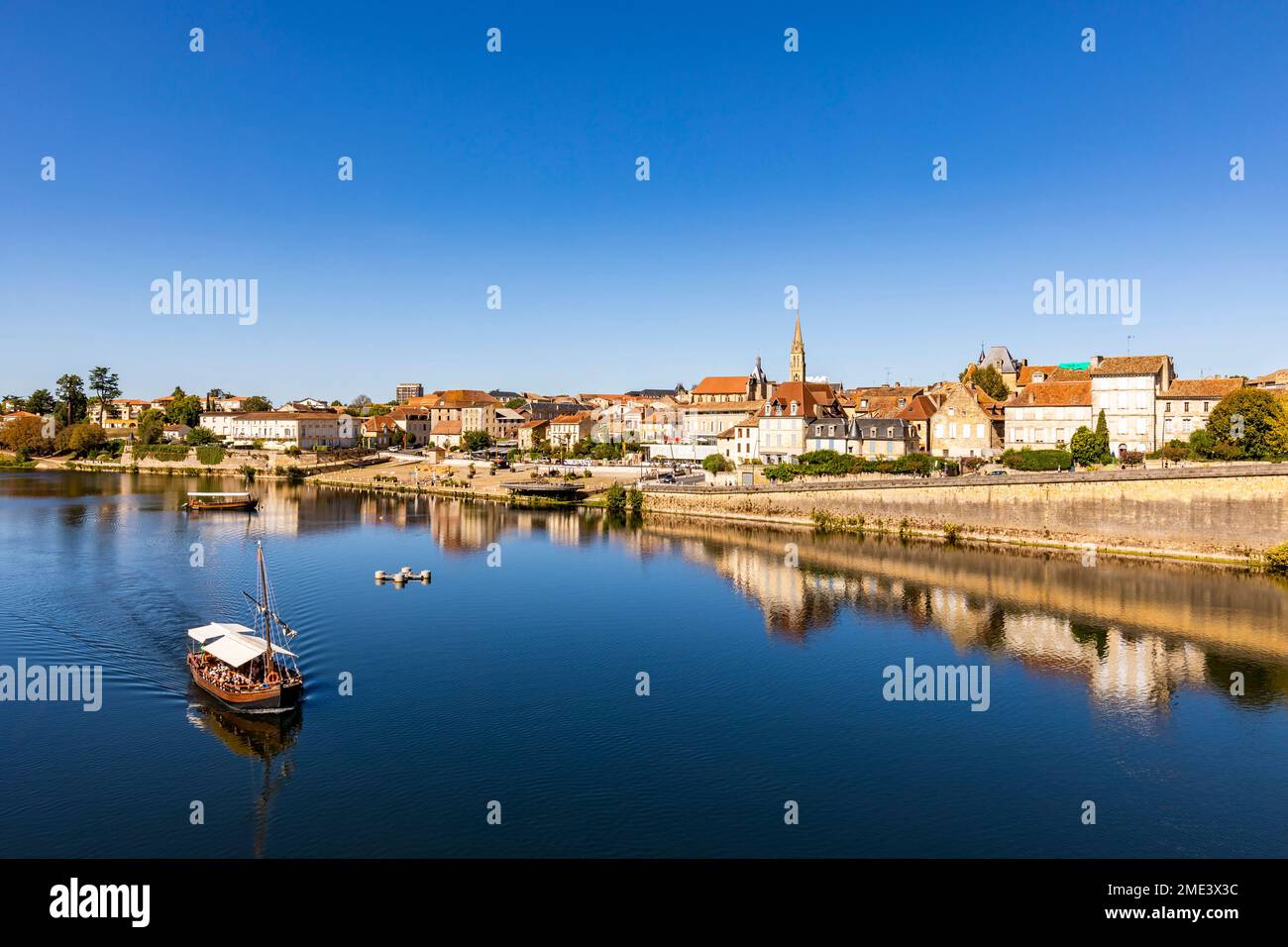 France, Nouvelle-Aquitaine, Bergerac, Boat sailing along Dordogne River with old town buildings in background Stock Photo