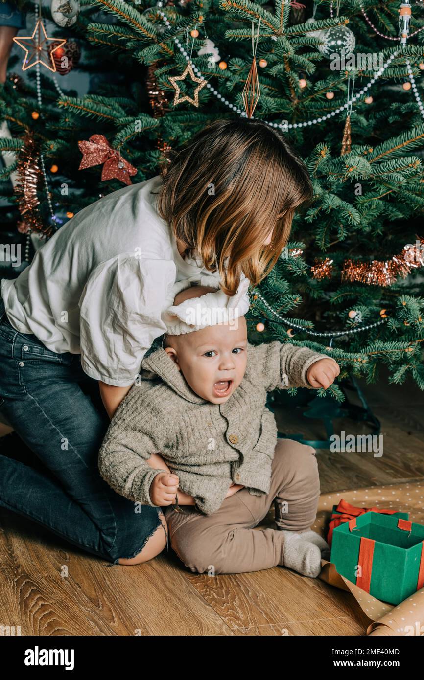 Sister playing with baby brother in front of Christmas tree Stock Photo