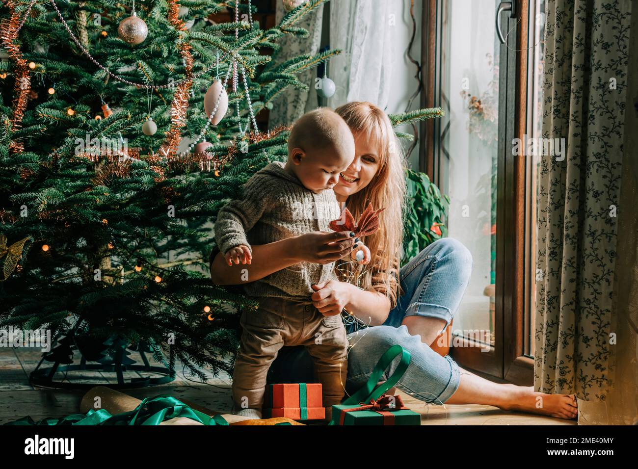 Happy mother playing with son in front of Christmas tree Stock Photo