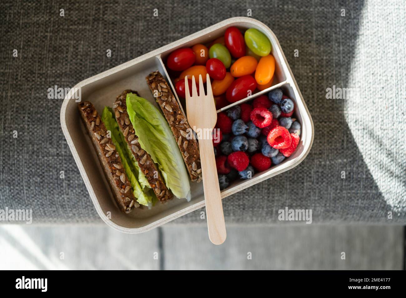 Rye bread, berries and salad with disposable fork in lunch box on sofa Stock Photo