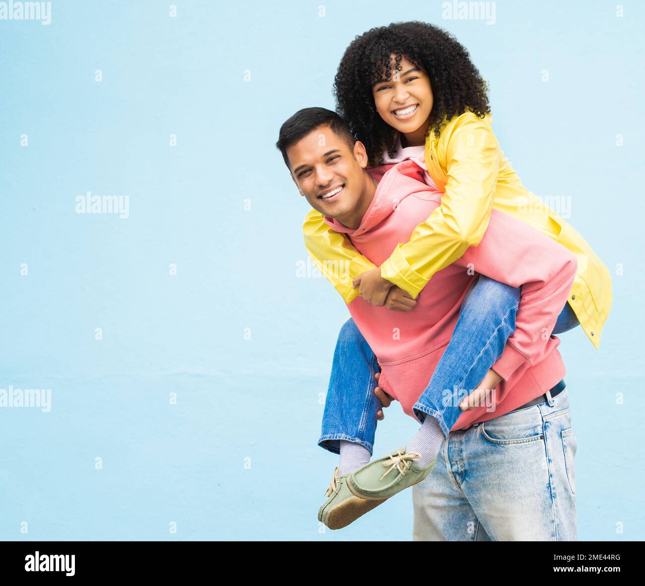 Happy couple, bonding or piggyback portrait on isolated blue background in city travel, date or fun game. Smile, happy man or carrying black woman in Stock Photo