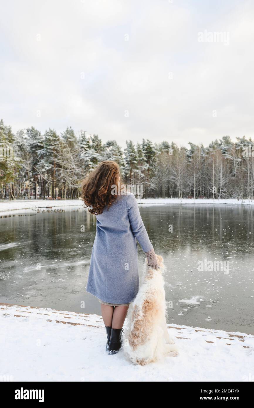 Mature woman standing with greyhound dog in front of frozen lake Stock Photo