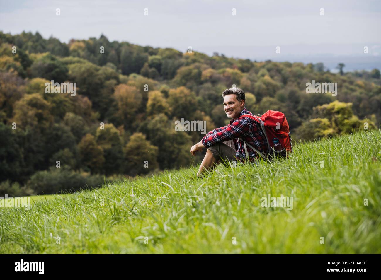Smiling man with backpack sitting on grass Stock Photo